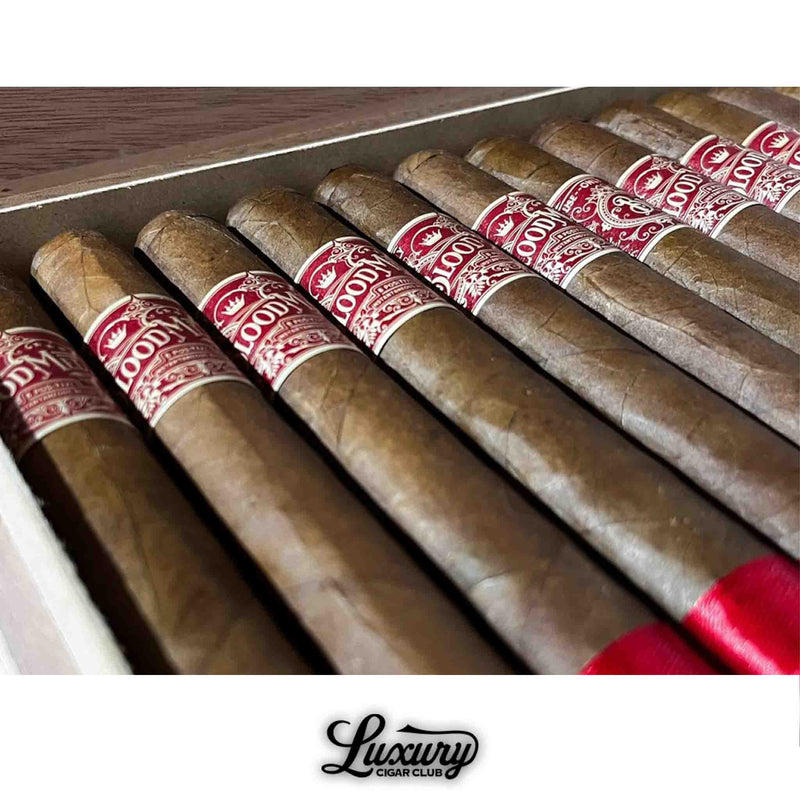 Close-up view of Crowned Heads Blood Medicine B Positive Limited Edition cigars inside an open box, showcasing detailed red cigar bands and red foot ribbons, with the Luxury Cigar Club logo beneath.