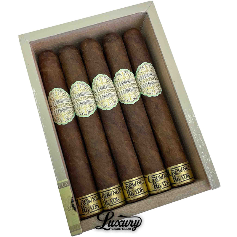 Close-up of Crowned Heads Le Pâtissier Cananazo cigars emphasizing the elegant band detail and oily Maduro wrappers. Cigars rest inside a cream-colored wooden box with Luxury Cigar Club logo beneath.