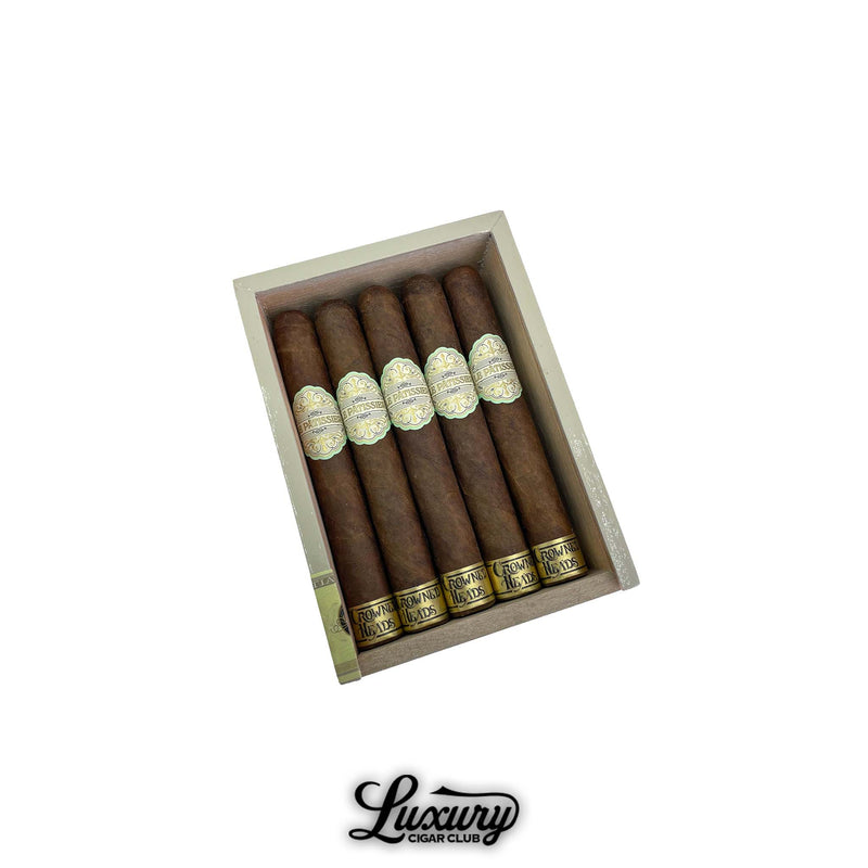 Open box of Crowned Heads Le Pâtissier Cananazo cigars featuring dark brown wrappers with ornate gold and ivory labels, arranged neatly in a cream-toned box. Luxury Cigar Club logo below.