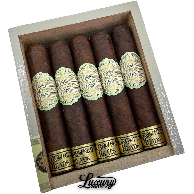 Close-up of Crowned Heads Le Pâtissier No. 50 cigars showing the fine texture of the Maduro wrappers and detailed band design. Displayed in a simple wood box with Luxury Cigar Club branding below.