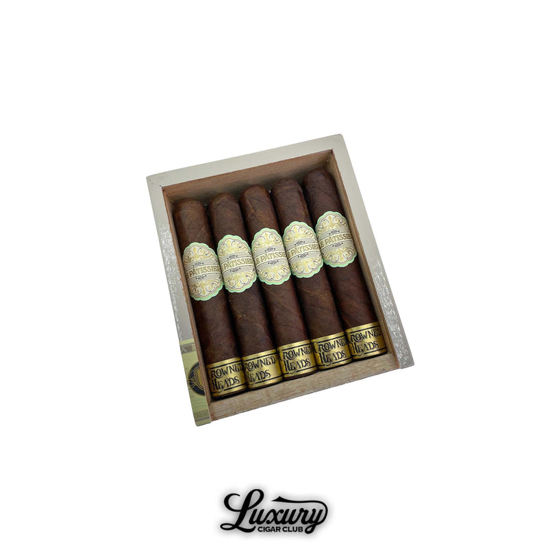 Open box of Crowned Heads Le Pâtissier No. 50 cigars arranged in rows, featuring dark wrappers and refined gold-accented bands. Luxury Cigar Club logo below.