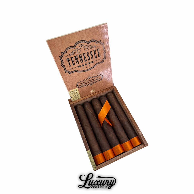 Open wooden box of Crowned Heads Tennessee Waltz Robusto Extra cigars with dark Maduro wrappers and orange foot ribbons displayed on a white background, Luxury Cigar Club branding