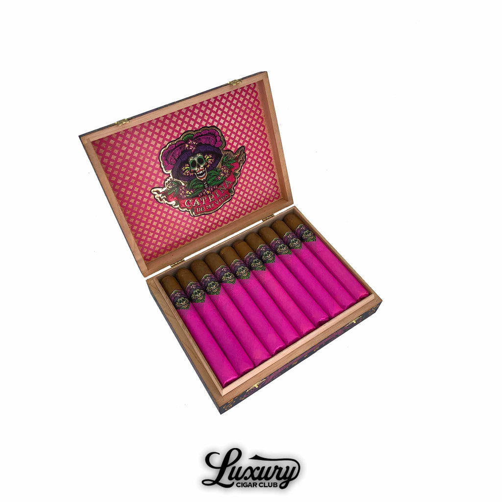 Open wooden box of Danli Honduras Catrina De Mi Vida Connecticut Toro cigars, featuring bright pink tissue wrapping and ornate gold and black skull bands. Luxury Cigar Club logo displayed below.