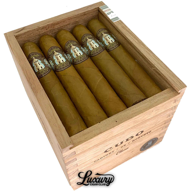 Close-up of Dapper Cubo Claro Robusto cigars inside a wooden box, emphasizing the smooth Connecticut wrappers and detailed Cubo bands depicting a white tower design with gold and teal accents. The refined presentation reflects premium Nicaraguan craftsmanship and sophisticated aesthetics. Luxury Cigar Club.
