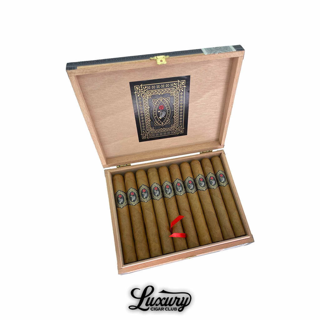 Open wooden box of Dapper La Madrina Shade Toro cigars showcasing a row of perfectly rolled, golden Connecticut-wrapped cigars. Each cigar features an ornate black and gold band with a red rose emblem, symbolizing elegance and refinement. The inside lid displays an intricate black and gold design, reflecting Dapper’s premium craftsmanship. The Luxury Cigar Club logo appears below. Luxury Cigar Club.