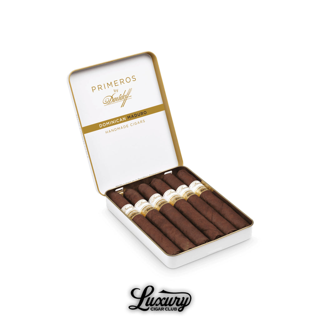 Open tin of Davidoff Primeros Dominican Maduro Petit Panatela cigars featuring dark brown wrappers and white bands with gold accents, displayed above the Luxury Cigar Club logo.