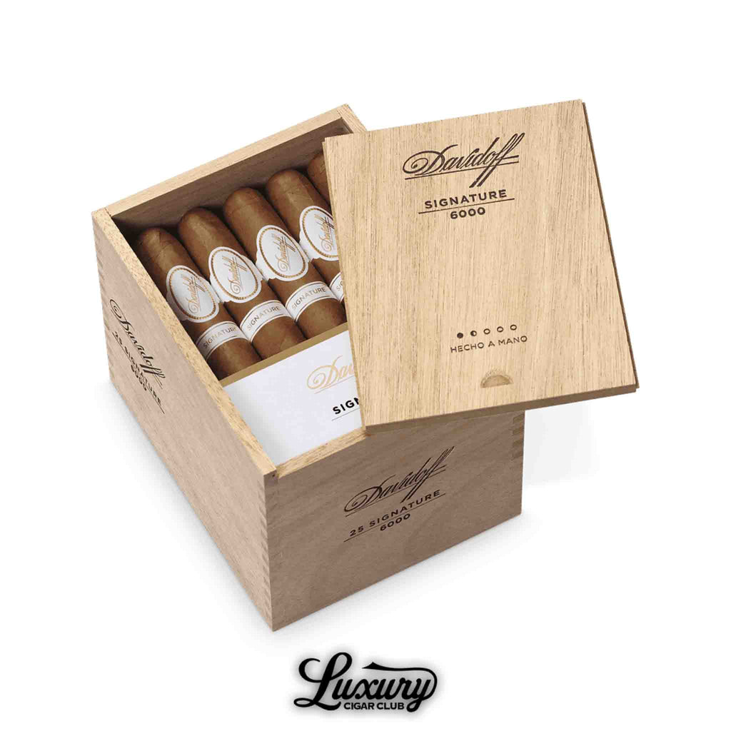 Open wooden box of Davidoff Signature 6000 cigars, showing neatly arranged cigars with white and gold bands, partially covered by a sliding lid engraved with “Davidoff Signature 6000,” and the “Luxury Cigar Club” logo beneath the box.