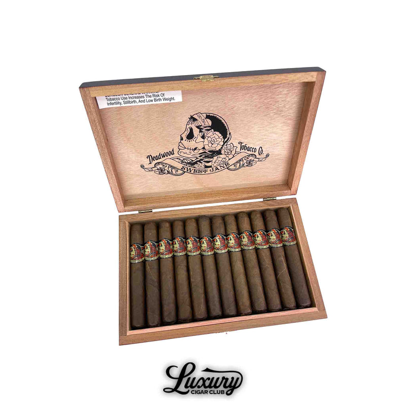 Open wooden box of Deadwood Sweet Jane Corona cigars from Drew Estate, featuring dark brown wrappers and colorful skull-themed bands. The inside lid displays the Deadwood Tobacco Co. logo. Luxury Cigar Club logo below.