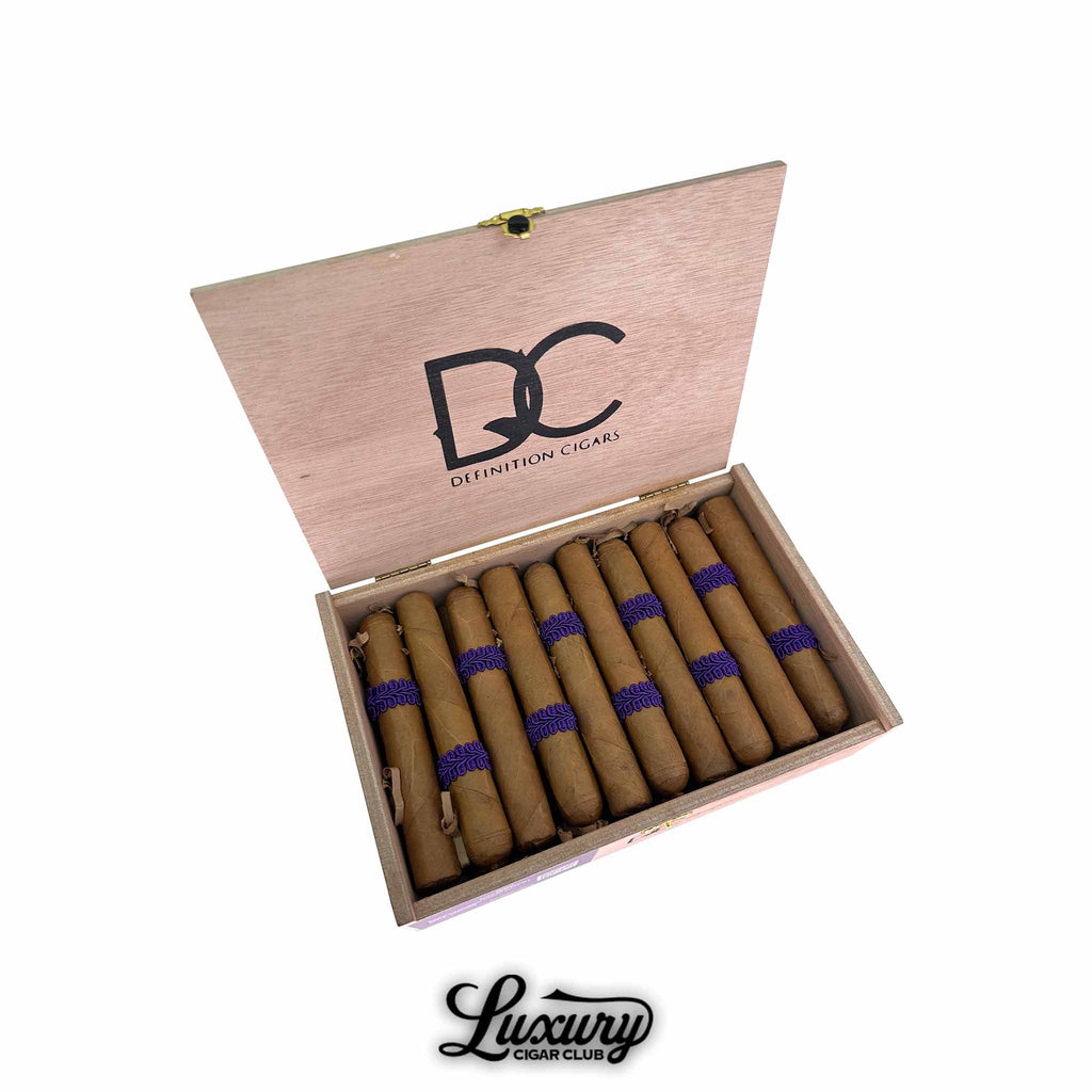Open wooden box of Definition Cigars Noir Connecticut Robusto showcasing cigars wrapped in golden Connecticut leaf with distinctive purple braided bands. The Definition Cigars logo is displayed on the inside lid. Luxury Cigar Club logo below.