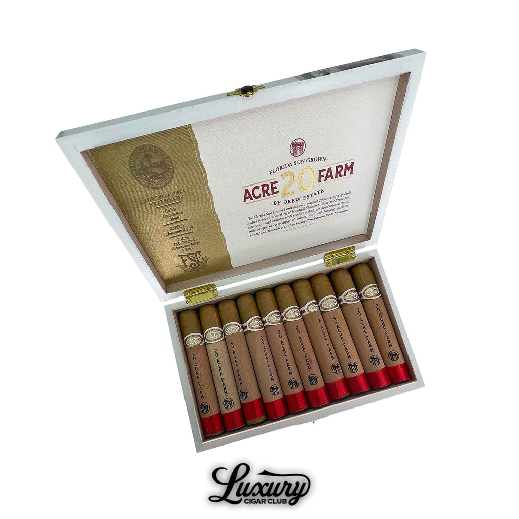 Open white box of Drew Estate 20 Acre Farm Robusto cigars featuring Connecticut shade wrappers and cedar sleeves with red foot bands. The inside lid displays blend details and branding. Luxury Cigar Club logo below.