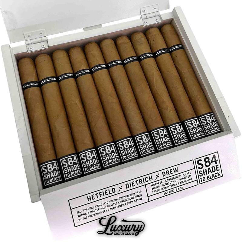 Close-up of Drew Estate Blackened S84 Shade to Black Toro cigars in a white box. The cigars display golden Connecticut wrappers with black “S84 Shade to Black” and “Blackened” bands. Luxury Cigar Club logo visible.
