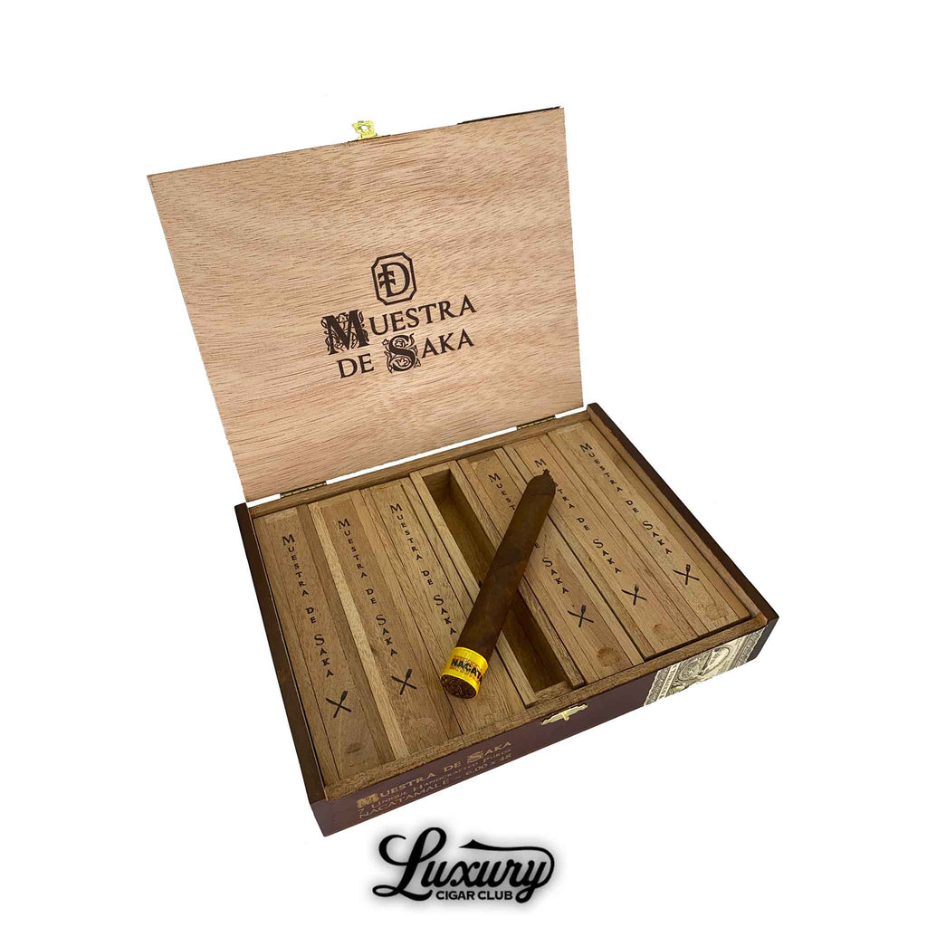 Dunbarton Tobacco & Trust Muestra de Saka Nacatamale cigar displayed in an open wooden box with individual cedar slots and branded lid, featured by Luxury Cigar Club.