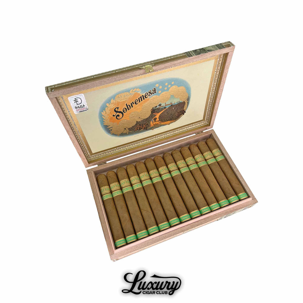 Open wooden box of Dunbarton Tobacco & Trust Sobremesa Brûlée Blue Wagashi Toro cigars, showcasing a neatly arranged row of golden Connecticut-shade wrapped cigars with elegant green and gold bands. The box interior features vintage artwork with “Sobremesa” branding, highlighting the premium craftsmanship and presentation. Luxury Cigar Club.