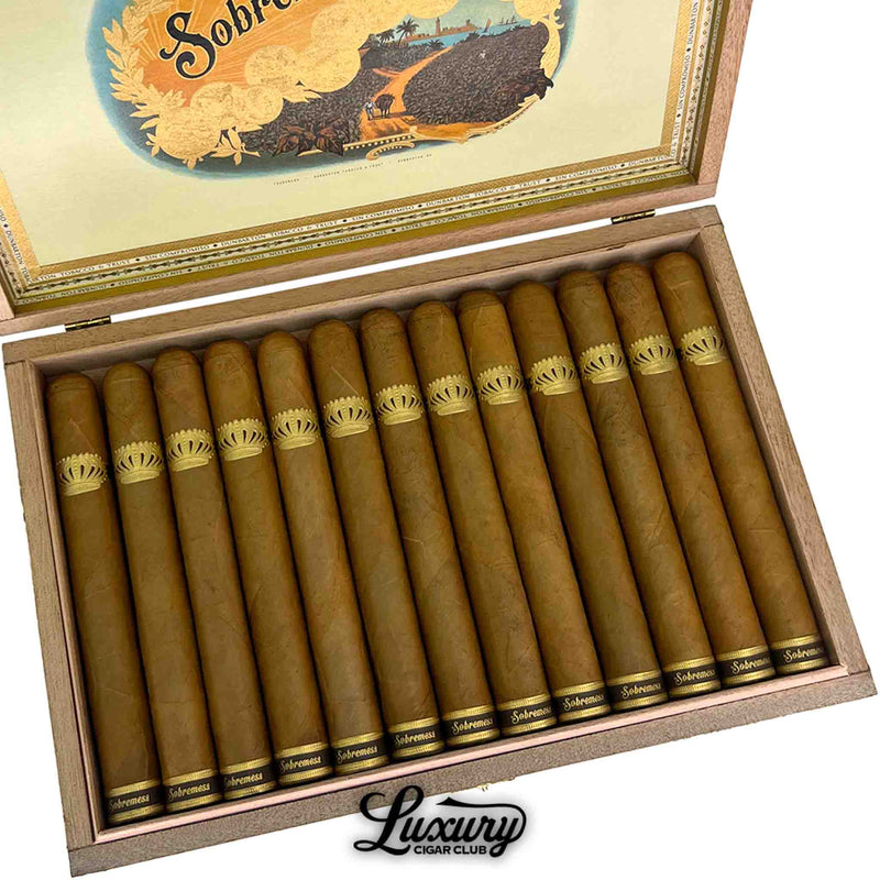Close-up of Dunbarton Tobacco & Trust Sobremesa Brûlée Double Corona cigars arranged in a box with light Connecticut wrappers and ornate gold crown bands. Luxury Cigar Club logo below.