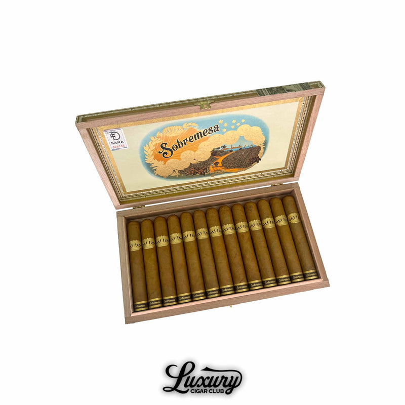 Open wooden box of Dunbarton Tobacco & Trust Sobremesa Brûlée Robusto cigars featuring golden Connecticut wrappers and ornate crown-shaped gold bands. Colorful Sobremesa artwork on the lid. Luxury Cigar Club logo beneath.