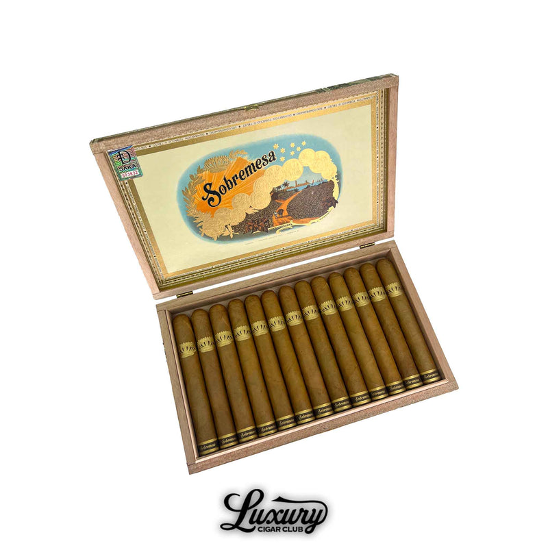 Open box of Dunbarton Tobacco & Trust Sobremesa Brûlée Toro cigars with light Connecticut wrappers and intricate gold crown bands, presented under the signature Sobremesa lid artwork. Luxury Cigar Club logo below.