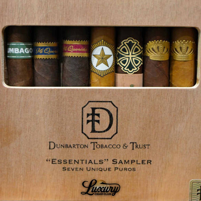 Close-up view of the Dunbarton Tobacco and Trust Essentials Sampler highlighting seven distinctive cigars arranged behind the box’s clear window, featuring visible cigar bands such as Umbagog, Mi Querida, Triqui Traca, StillWell Star, Sin Compromiso, Sobremesa, and Sobremesa Brûlée, captured for Luxury Cigar Club.