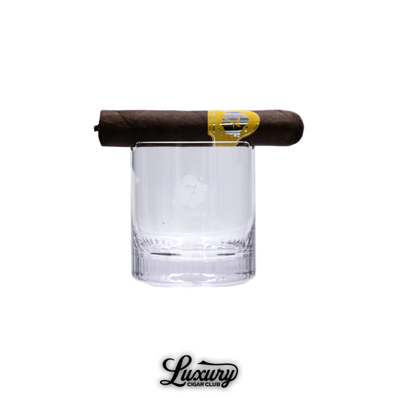 Premium clear whiskey glass featuring the El Septimo logo etched on the front, designed with a built-in cigar holder slot, shown with a brown cigar resting on top.