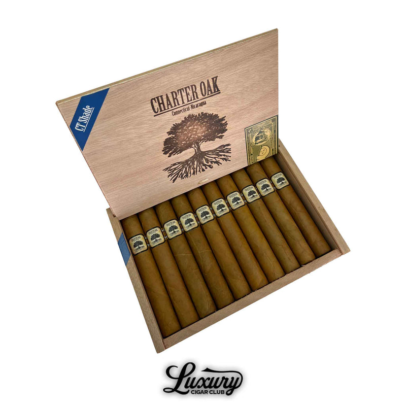 Open box of Foundation Charter Oak Connecticut Shade Grande cigars, featuring 10 light brown cigars neatly arranged in rows. The wooden lid displays a large oak tree graphic with “Charter Oak Connecticut Nicaragua” text and a blue CT Shade corner label, with “Luxury Cigar Club” branding at the bottom.