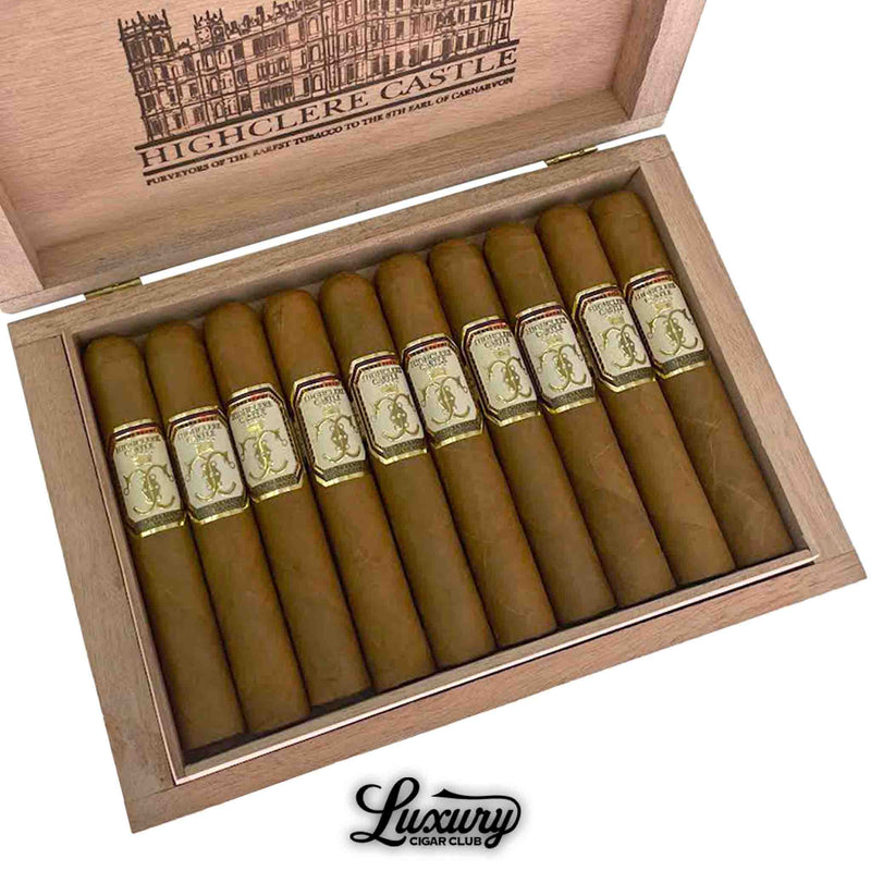 Close-up of a box of Foundation Highclere Castle Edwardian Robusto cigars, showing 10 well-packed light brown cigars with ornate cream, gold, and red bands. The lid interior features a detailed Highclere Castle illustration and branding, with “Luxury Cigar Club” logo visible beneath the box.
