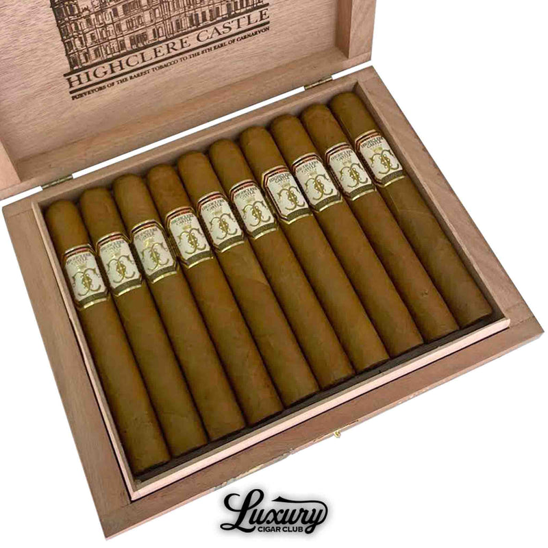 Close-up of an open box of Foundation Highclere Castle Edwardian Toro cigars, showing 10 neatly arranged light brown cigars with elegant cream, gold, and red bands. The box lid displays a detailed illustration of Highclere Castle and branded text, with “Luxury Cigar Club” logo at the bottom.