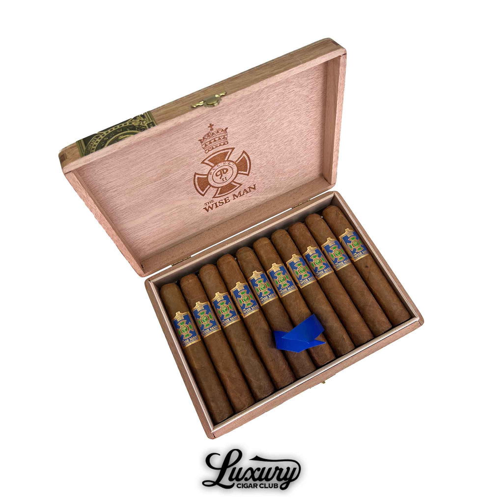 Open wooden box of Foundation The Wise Man Corojo Corona cigars from Luxury Cigar Club. The cigars feature a light brown wrapper with vibrant blue and gold bands. A blue ribbon rests across the cigars for a polished presentation, with “The Wise Man” logo engraved inside the box lid.