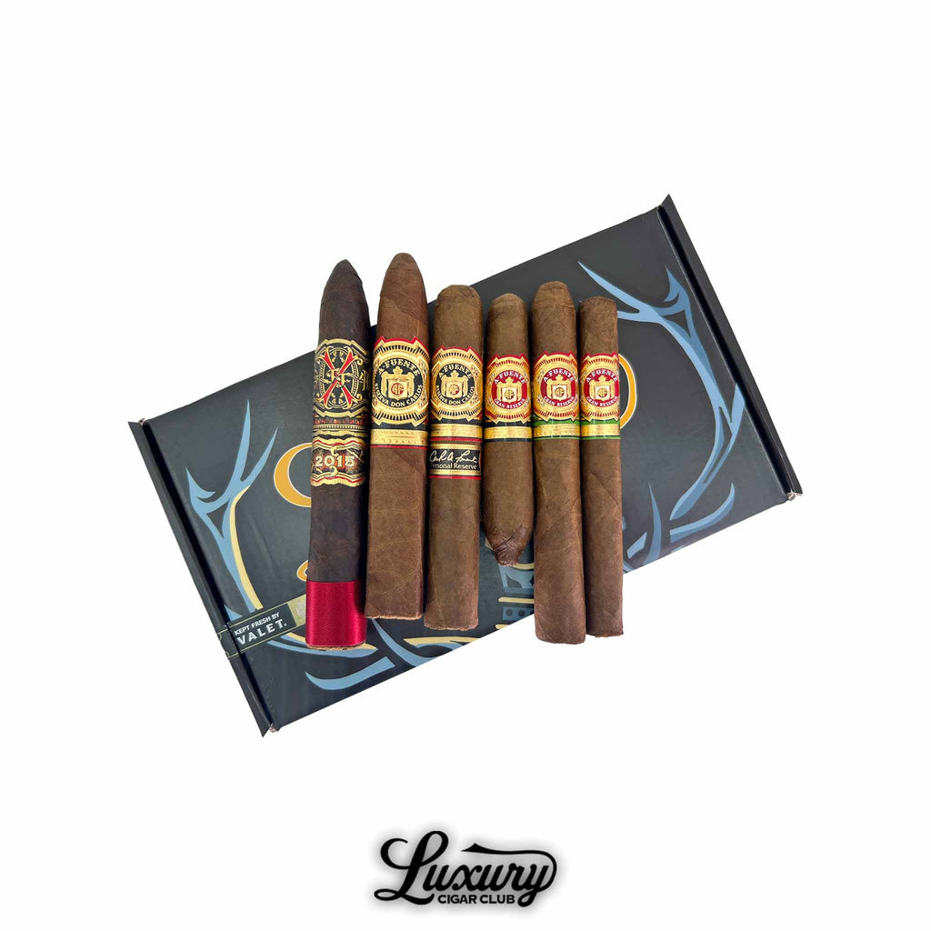 Fuente Family Royal Collection Sampler featuring six premium Arturo Fuente cigars displayed on a black presentation box with gold and blue detailing, photographed by Luxury Cigar Club.
