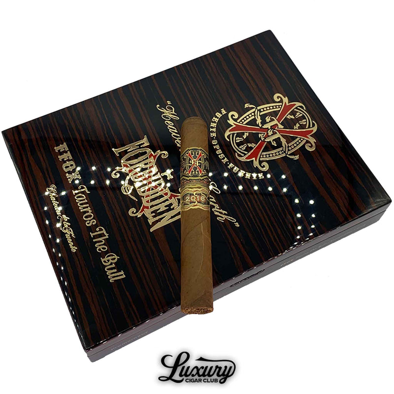 Close-up of a Fuente Fuente Opus X Heaven and Earth Tauros the Bull Natural Toro cigar resting on a glossy dark wood grain box with gold and red embossed branding and “Forbidden” script.
