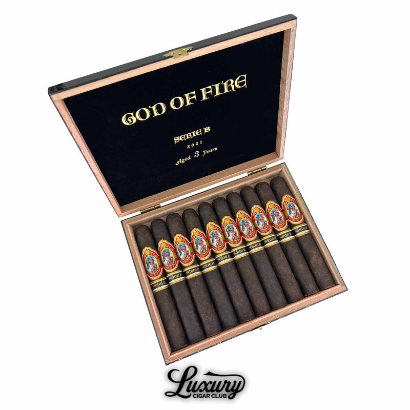 Box of God of Fire Serie B Double Robusto cigars from 2021, aged 3 years, featuring dark wrappers and vibrant red, gold, and black cigar bands with classical artwork, elegantly arranged in a black velvet-lined wooden box with Luxury Cigar Club branding.