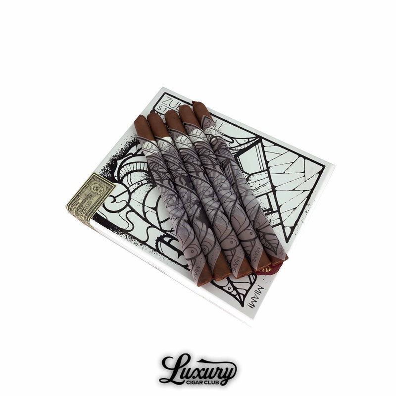 Five Gran Habano Zulu Zulu Mas Paz cigars displayed on top of a white, black-illustrated box featuring abstract artwork. Each cigar is wrapped in a striking, art-inspired sleeve with bold geometric designs, highlighting the collaboration with artist Mas Paz. The cigars feature dark brown wrappers and a refined tapered foot. The Luxury Cigar Club logo appears below. Luxury Cigar Club.