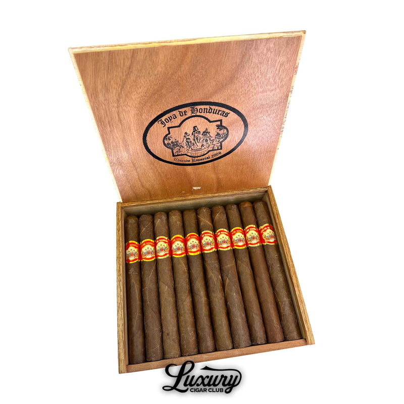 Open wooden box of Joya de Honduras Churchill cigars from Luxury Cigar Club, displaying twelve long cigars with deep brown wrappers and signature red and gold bands.