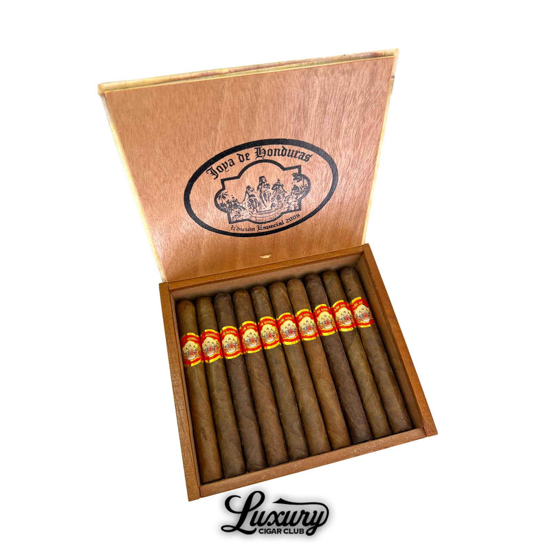 Open box of Joya de Honduras Corona cigars from Luxury Cigar Club, showing twelve perfectly rolled handmade cigars with red and gold bands resting in a cedar box.