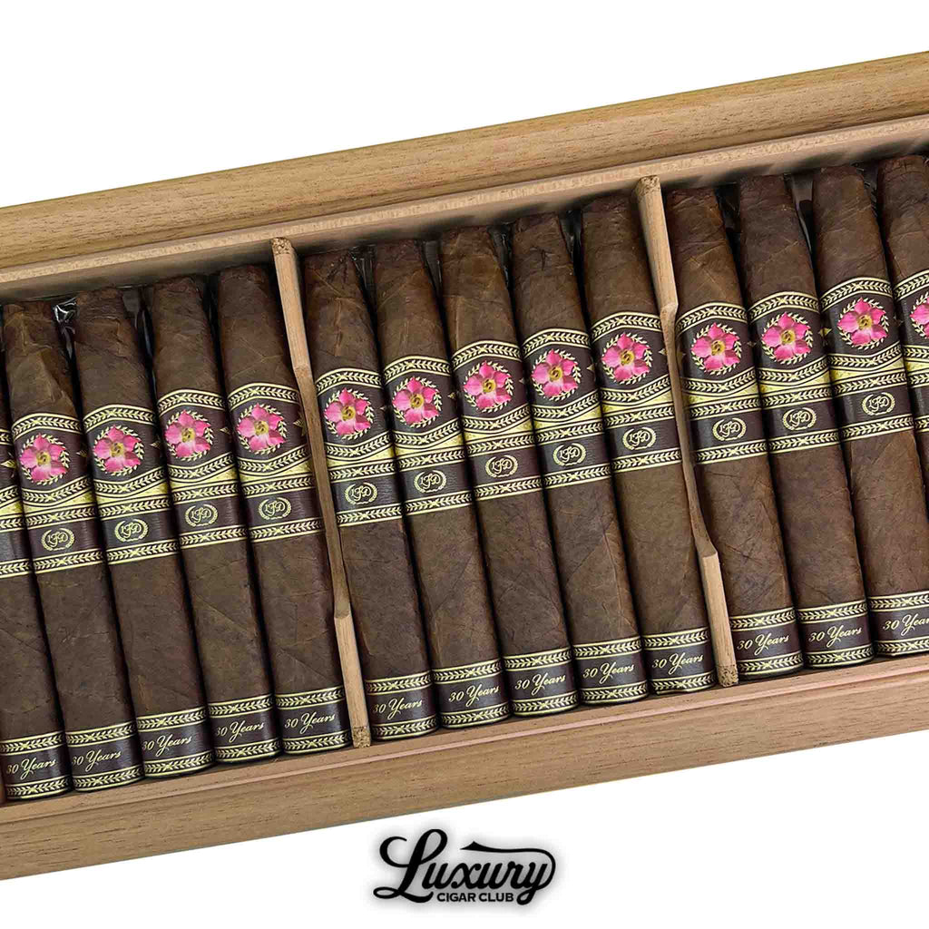 Open wooden box of La Flor Dominicana 30th Anniversary Chisel cigars with pink and gold bands, displayed with Luxury Cigar Club logo.