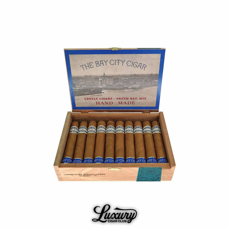 Open box of Lovely Cigars The Bay City Cigar Connecticut Robusto cigars, showing golden-brown wrappers with silver and blue bands. The inside lid features vintage artwork labeled “The Bay City Cigar” and “Hand Made.” Luxury Cigar Club logo below.