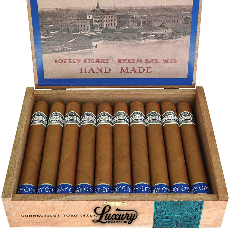Close-up of Lovely Cigars The Bay City Cigar Connecticut Toro cigars with smooth golden wrappers and silver-blue “Lovely Cigars” bands in a wooden box. Vintage Green Bay artwork visible on the lid. Luxury Cigar Club logo beneath.