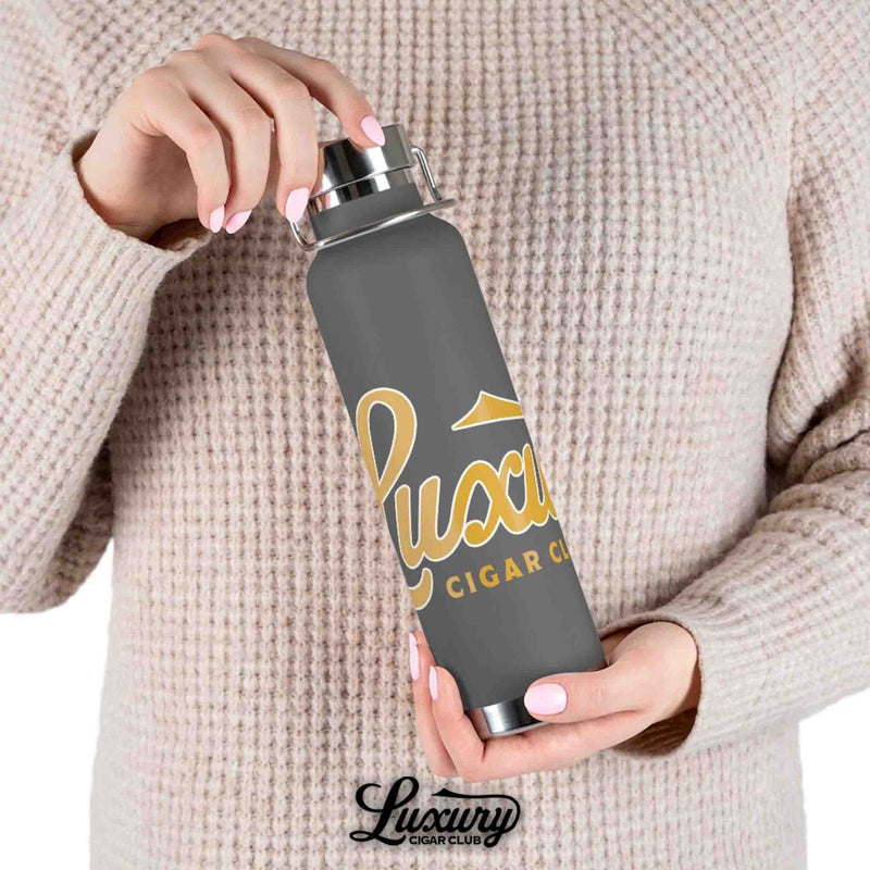 Luxury Cigar Club copper vacuum insulated 22oz bottle in matte grey with gold logo held in hand lifestyle photo