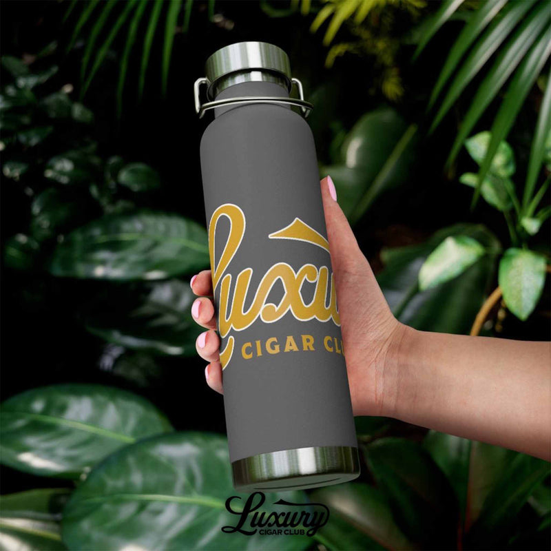 Luxury Cigar Club copper vacuum insulated 22oz bottle in matte grey with gold logo photographed outdoors with plants