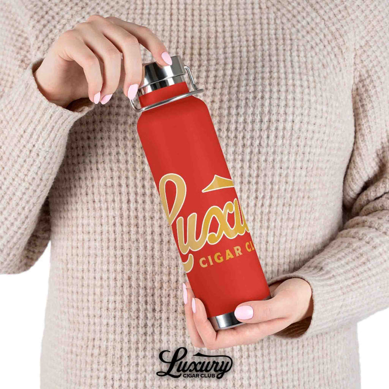 Hand holding Luxury Cigar Club copper vacuum 22oz insulated bottle in red with gold logo lifestyle view against sweater background