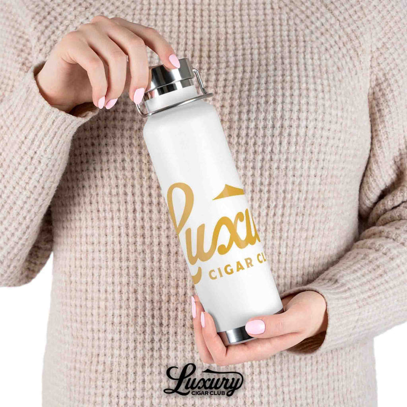 Luxury Cigar Club copper vacuum insulated bottle in white held by person wearing knit sweater showing gold logo
