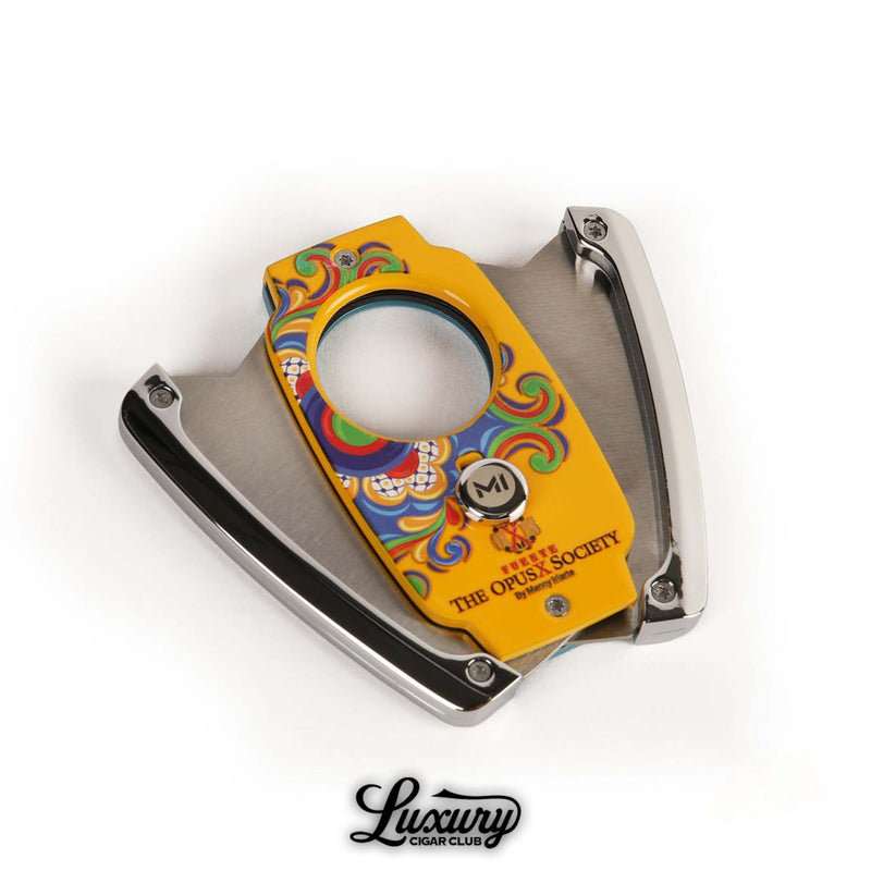 Close-up of Manny Iriarte Opus X Society Colonial Tiles Cutter laying open to reveal precision stainless steel blades and vivid multicolor artwork, photographed for Luxury Cigar Club.