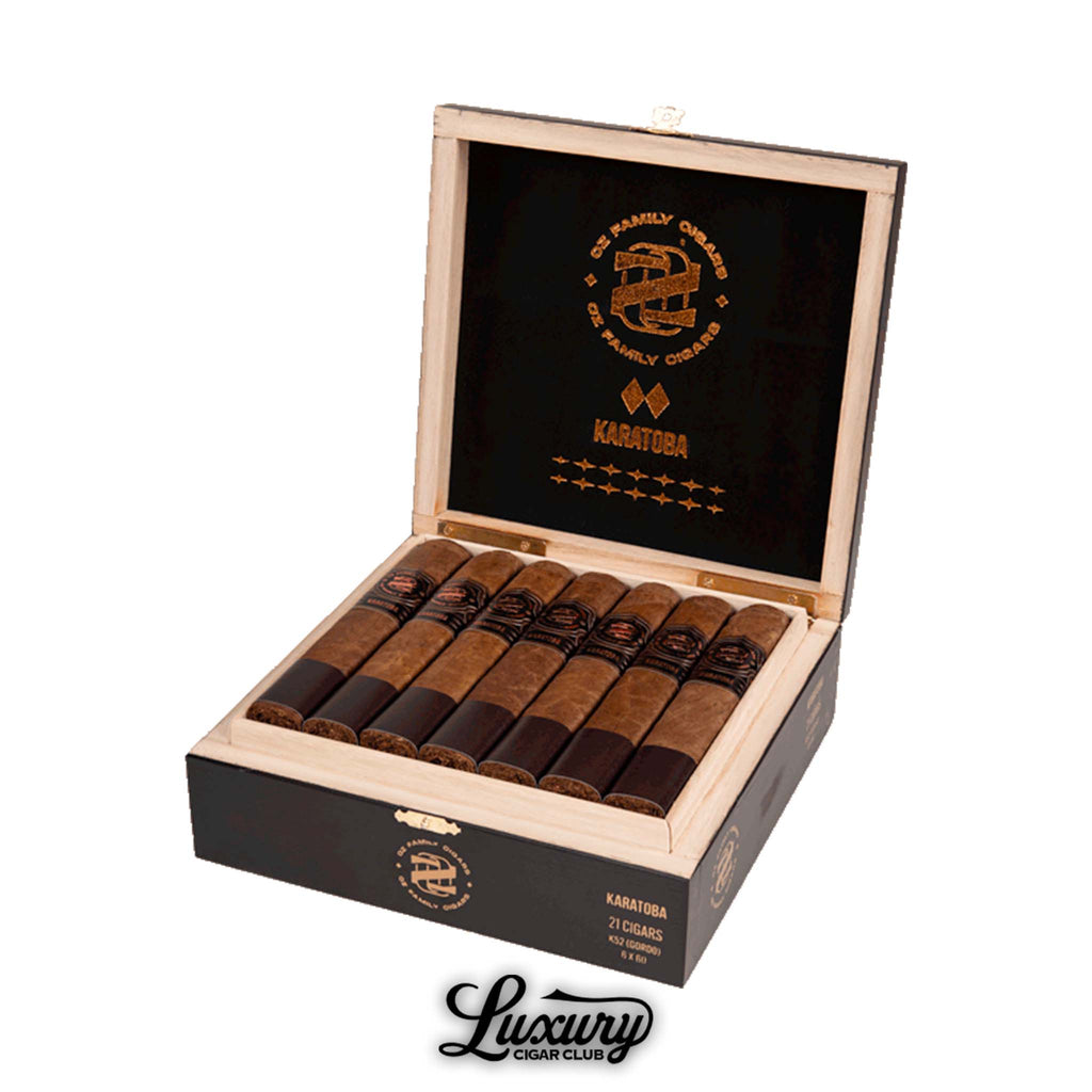 Open box of Ozgener Family Cigars Karatoba Robusto cigars, showing 21 hand-rolled cigars with dark brown wrappers and copper-accented black bands, inside a black-and-wood box marked with the Karatoba logo and branding, displayed above the Luxury Cigar Club logo.