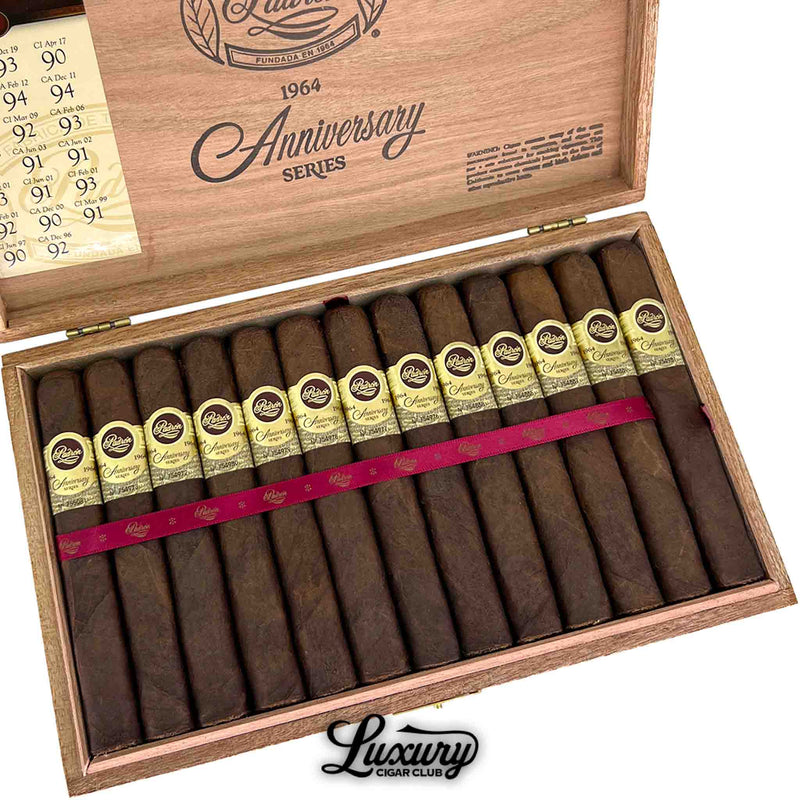 Close-up of Padron 1964 Anniversary Series Maduro Exclusivo cigars in their box, highlighting detailed gold bands and rich Maduro wrappers under warm wood tones. Luxury Cigar Club logo below.