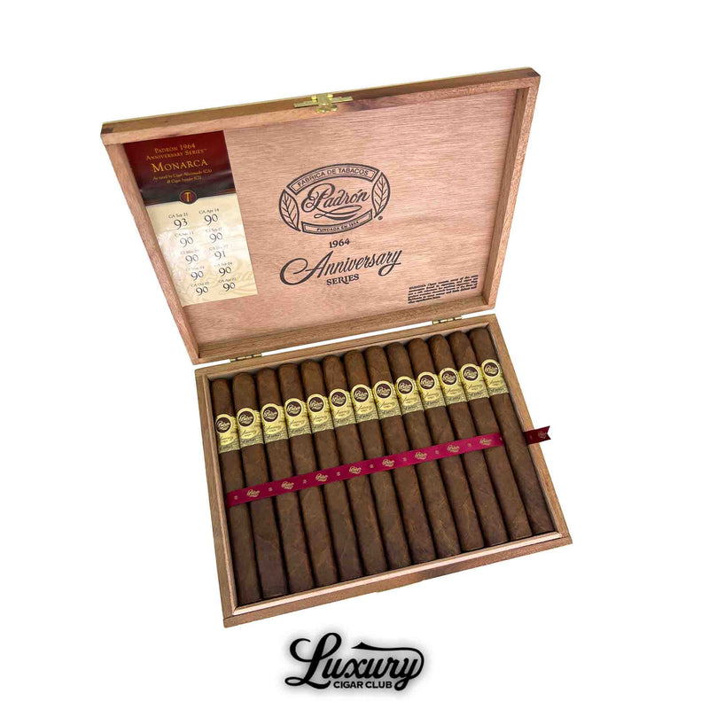 Open wooden box of Padron 1964 Anniversary Series Maduro Monarca cigars, neatly arranged with gold and brown bands, secured by a red ribbon, and featuring high-rating labels inside the lid. Luxury Cigar Club branding below.