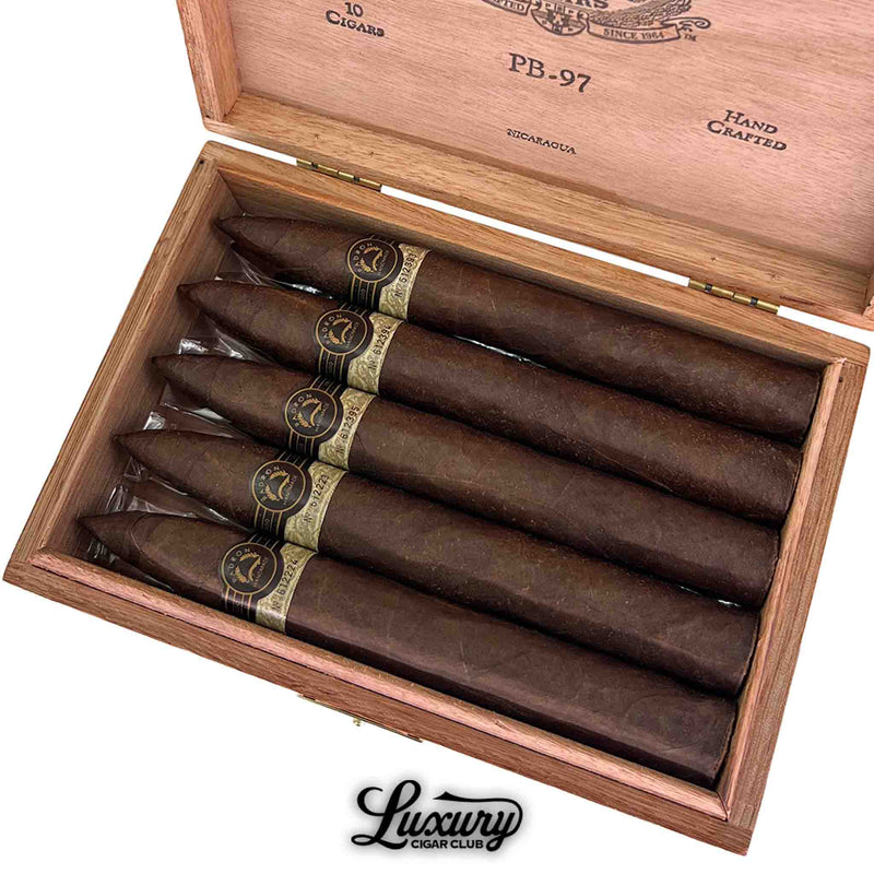 Close-up of Padron Black Maduro Unicorn PB97 box showing six dark cigars with gold and black bands inside wooden box, Luxury Cigar Club logo at bottom.