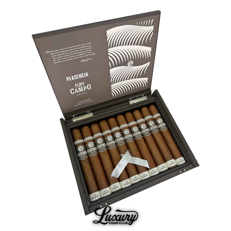 Open box of Plasencia Alma del Campo Madroño cigars featuring ten large, smooth brown cigars with white and silver bands, arranged neatly in a sleek dark wood box with artistic leaf patterns on the inner lid and Luxury Cigar Club logo below.