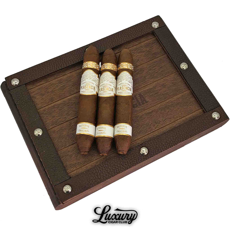 Close-up of Plasencia Reserva Original Cortez cigars resting on a dark wooden box with metal rivets, highlighting premium organic Nicaraguan tobacco — Luxury Cigar Club.