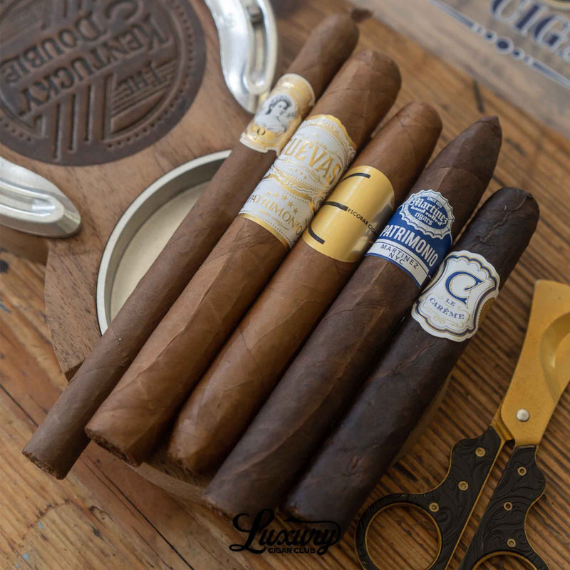 Set of five cigars from the Luxury Cigar Club Platinum Subscription resting on a wooden ashtray, including blends from Cuevas, E.P. Carrillo, and Crowned Heads.
