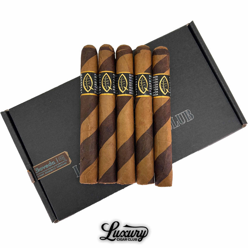 Close-up of Quesada Aged Reserva Privada Corona Gorda cigars showing dual-tone barber pole wrappers in dark and light brown hues. Cigars rest on a black Luxury Cigar Club box with gold-accented Quesada branding.