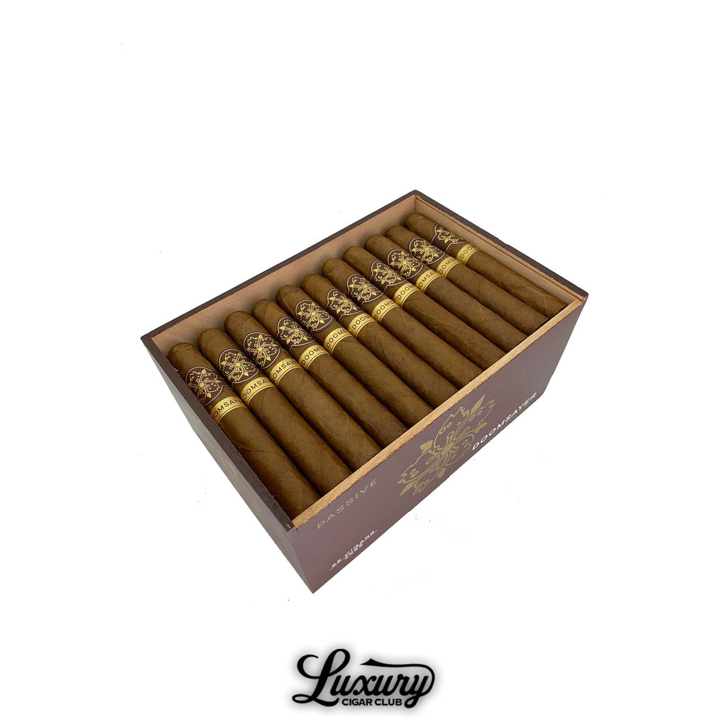 Open box of Room101 Doomsayer Passive Claro cigars neatly arranged in rows with brown wrappers and gold embossed cigar bands.
