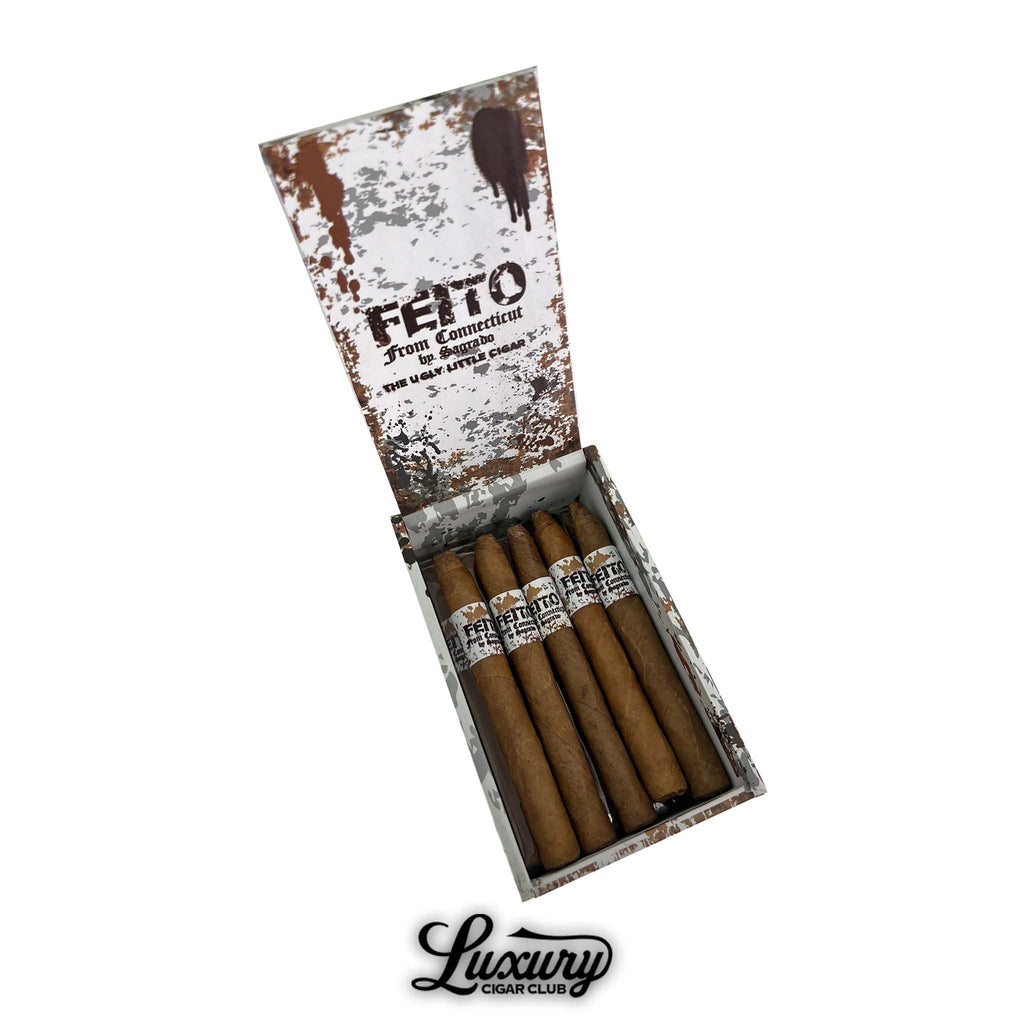 Open box of Sagrado Feito From Connecticut Panatela cigars featuring rustic white-and-brown distressed artwork on the lid. Cigars displayed in a row with white speckled bands labeled “Feito From Connecticut.” Luxury Cigar Club logo below.